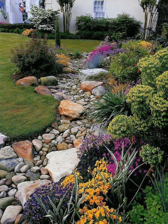a dry river bed with pebbles and larger pieces of rocks and grass and bright blooms lining up