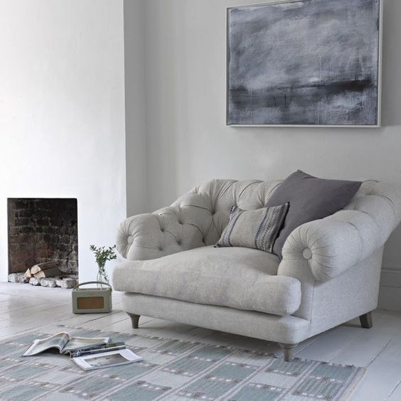 a grey overstuffed chair and pillows by the fireplace is one of the comfiest places to read in