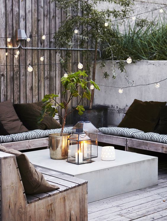 A welcoming outdoor lounge with an U shaped banquette and a concrete coffee table plus lights all over