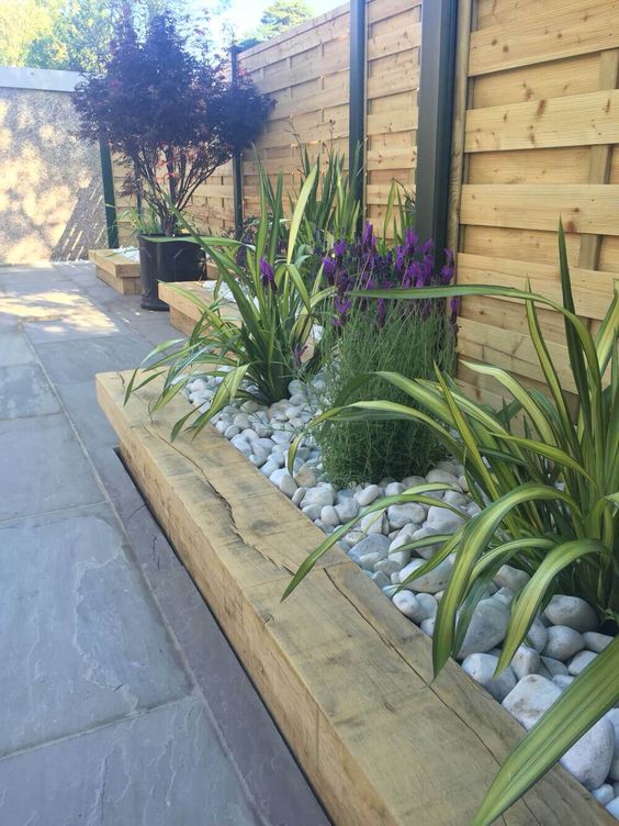 a wooden garden bed edge, bright flowers and greenery all covered with neutral pebbles on top