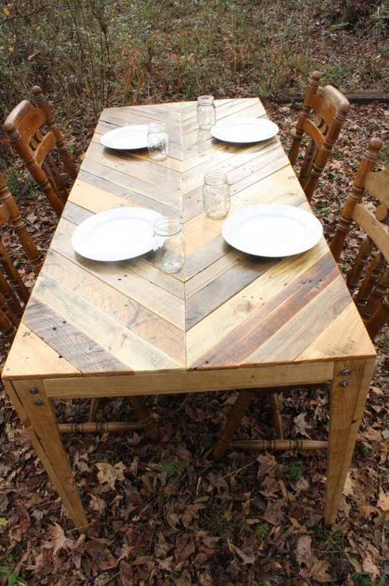 an outdoor dining table with a chevron pattern on the tabletop fully built of pallet wood and vintage chairs