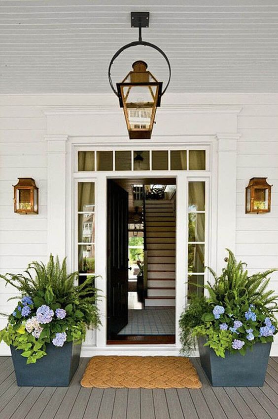 graphite grey planters with lush greenery and bright blooms line up the door and give the porch a fresh feel