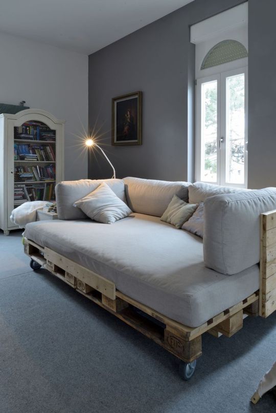 a pallet daybed with a back and casters, fitted with a comfy mattress and pillows on top