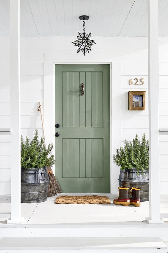 a sage green door matches the greenery that is growing in the large milk churns