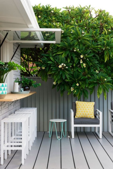 A garage style window with a wooden windowsill outdoors, white plank stools and a grey wooden deck