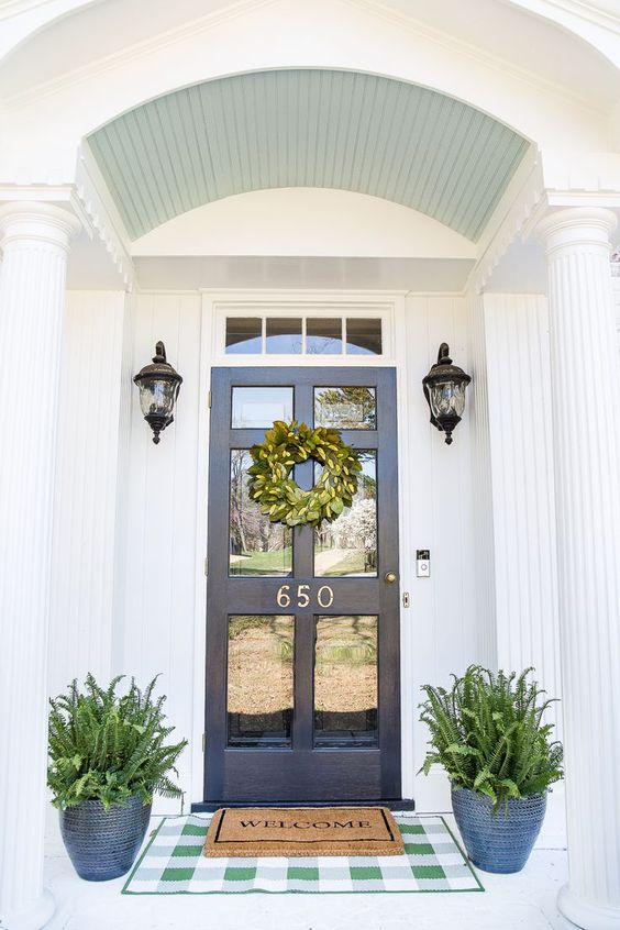 a navy door with glass, navy patterned planters with ferns and vintage lamps over the pots