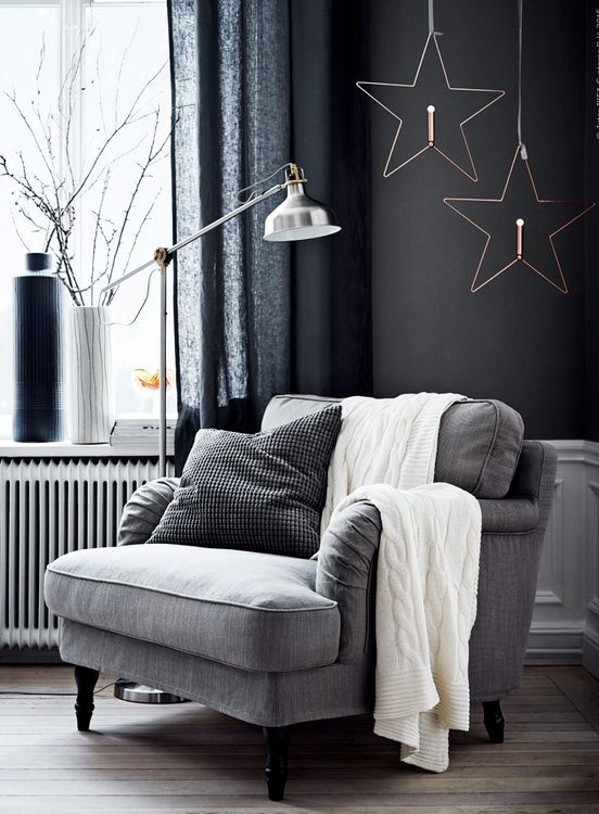 a simple grey upholstered chair by the window, a metal floor lamp, pillows and a knit blanket