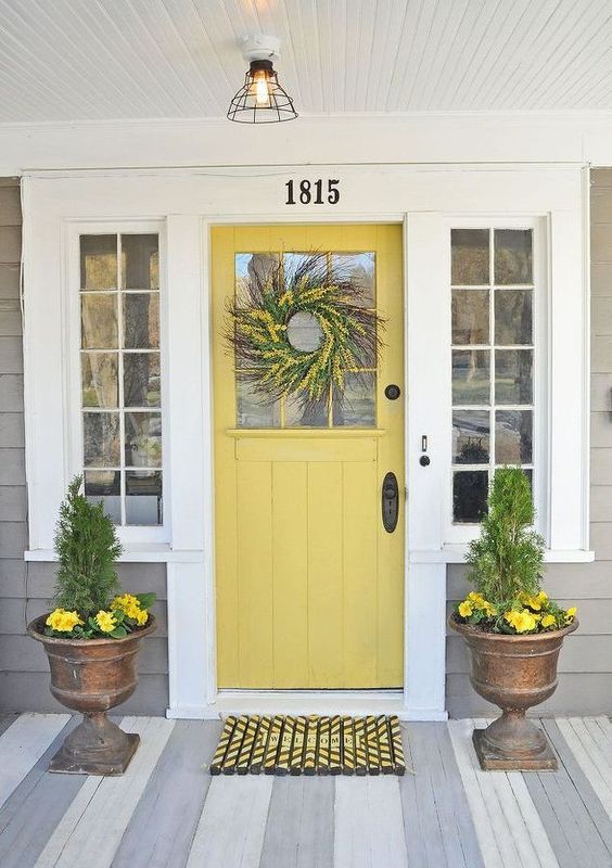 a mustard farmhouse door, antique stone urns with greenery and yellow blooms to match the door