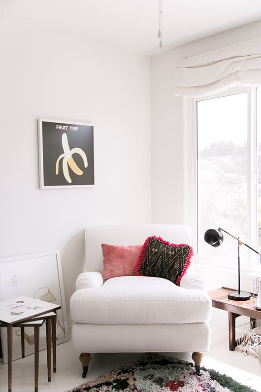 a white overstuffed chair with pillows by the window is a cool furniture piece to read on
