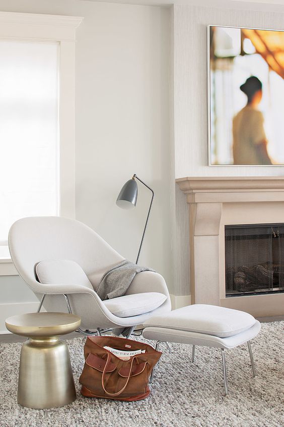 A comfy mid century inspired white chair and a matching footrest, a metal floor lamp and a metal side table for a comfy nook