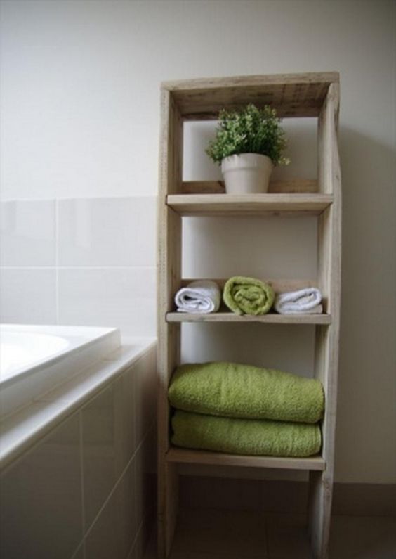 a bathroom shelving unit with several tiers for storign towels and some potted greenery built of pallets