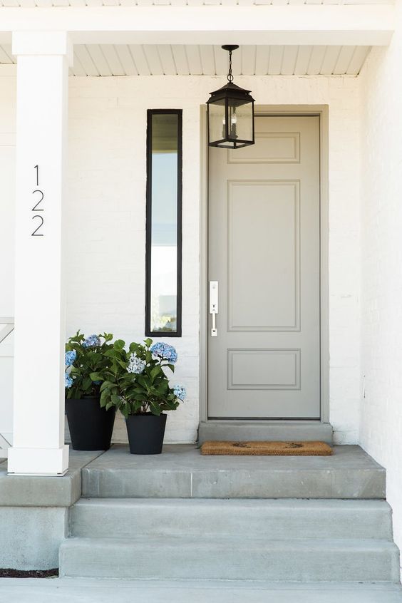 a dove grey door, a vintage lamp and a duo of black planters with blue flowers create a cozy vintage-inspired porch