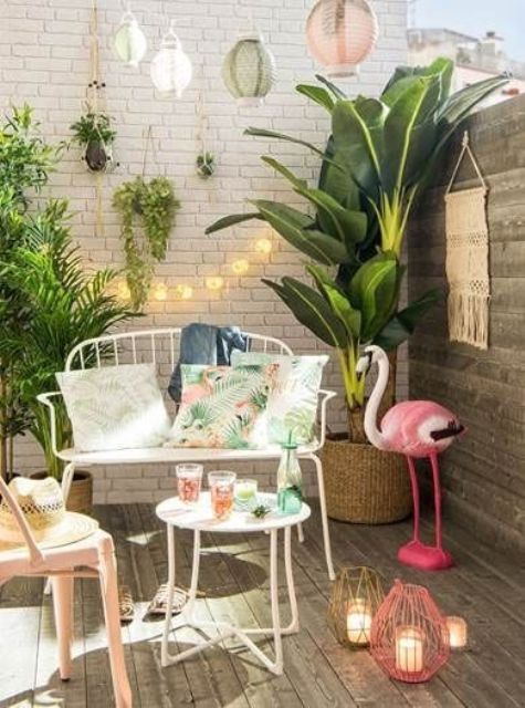 a mini tropical deck with potted greenery, a pink flamingo, colorful candle lanterns, elegant white forged furniture and lights
