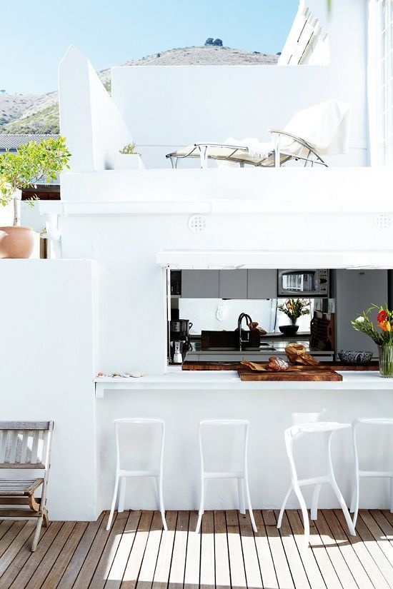 a roll up window, a white tabletop and white stools for a bright minimalist outdoor space
