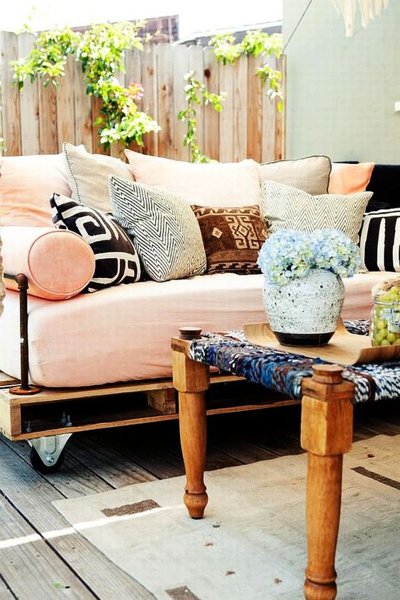 an outdoor pallet daybed on casters with a soft mattress and lots of colorful and printed pillows