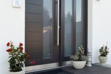 20 a large contemporary door with glass inserts, three planters with blooms and greenery on the porch