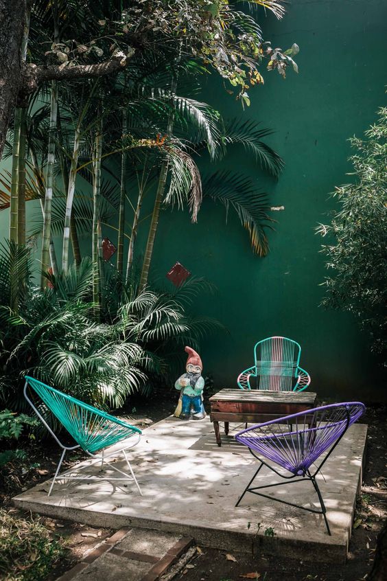 a simple tropical patio with colorful chairs, a vintage wooden table and lots of tropical plants growing aroud