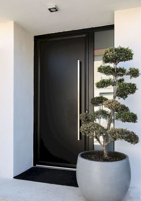 a large grey planter with a mini tree plus a laconic black door to make a chic minimalist porch