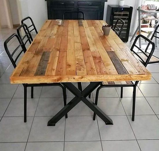 A stylish dining table with criss cross metal legs and a pallet wood tabletop and black metal chairs