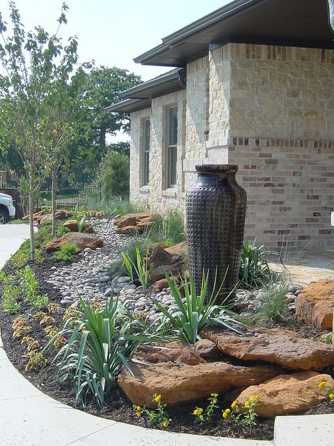 such a no flower front yard with a large vase fountain, rocks, agaves and grasses is a bold modern idea