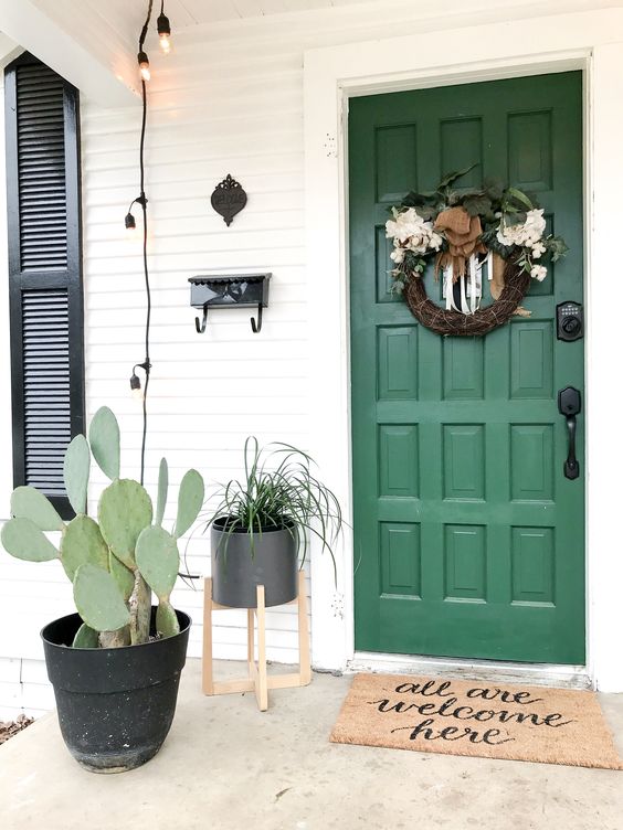 a planter with a cactus and a planter with greenery on a stand match the green door and a wreath adds charm