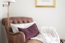 23 a vintage-inspired leather chair in brown with pillows and a knit blanket is always a good diea to try