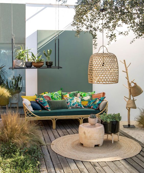 a welcoming tropical terrace with a rttan sofa, colorful pillows, a jute rug, wicker baskets and a wicker lampshade plus potted plants