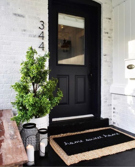 a white planter with a mini tree and black candle lanterns plus a black door for a stylish modern look