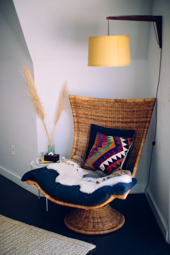 a woven chair on a stand with pillows, thrwos and blankets is a stylish idea for a boho space