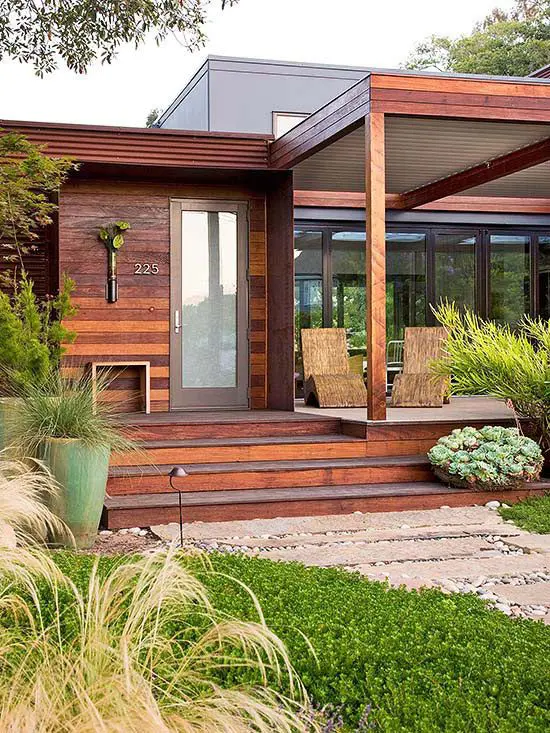 a beautiful modern front yard with a green lawn, grasses and greenery in tall planters plus a wooden deck