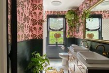 a bright eclectic bathroom with black wall paneling, pink wallpaper, a black vanity, a large mirror and potted greenery