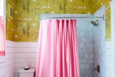 a bright eclectic bathroom with mustard wallpaper and bird print, a bathing space with a pink curtain and a pink curtain on the window, white planks and white marble tiles
