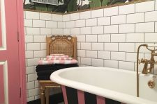 a brigth bathroom with white subway tiles, tropical leaf wallpaper, a striped bathtub, a pink door and a checked floor plus pop artworks