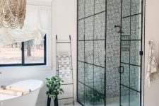 a catchy eclectic bathroom with printed tile in the shower, a tub by the window, a tile and laminate floor and a bead chandelier