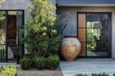 a chic and edgy modern front yard with greenery and trees, with an oversized shabby chic planter and stone garden paths