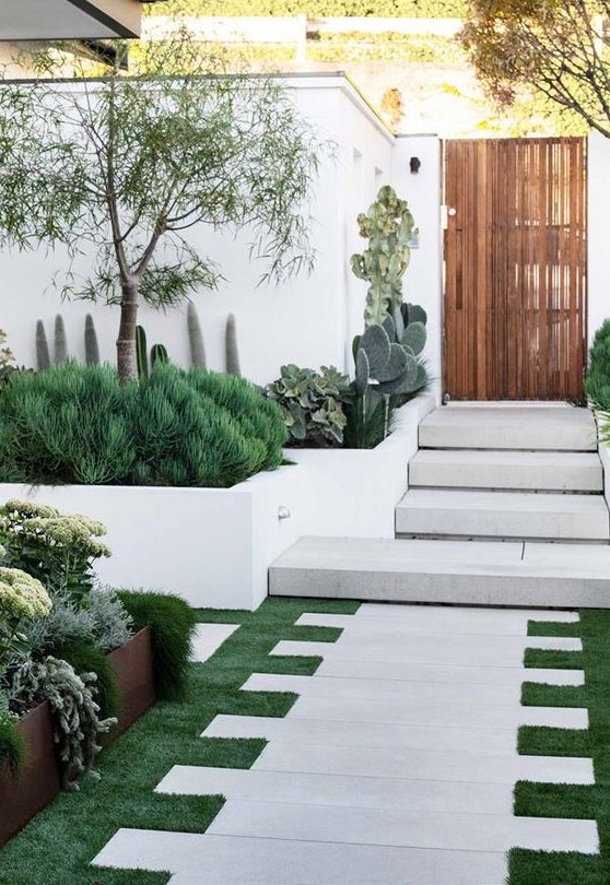 A jaw dropping front yard with grass and stone tiles, with greenery, cacti, trees and succulents is a very welcoming space