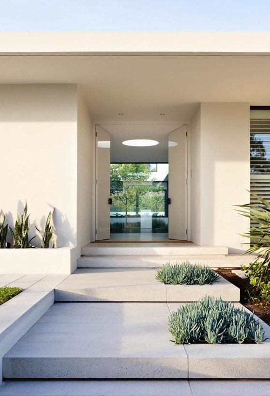 A modern front yard clad with stone tiles and with succulents and cacti growing right in the tables and in built in planters is very sleek and elegant