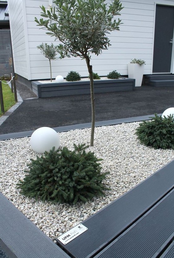 a modern front yard with a dark deck and neutral pebbles, greenery, trees and white balls plus elegant modern planters is a chic idea