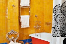 a super bold maximalist bathroom with bold yellow and blue tiles, colorful mosaic tiles on the floor, a red bathtub, a vintage chair
