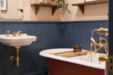a boho bathroom with white walls and navy paneling, a rust-colored bathtub, a wall-mounted sink and some open shelves