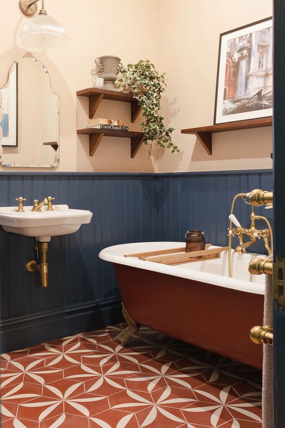 A boho bathroom with white walls and navy paneling, a rust colored bathtub, a wall mounted sink and some open shelves