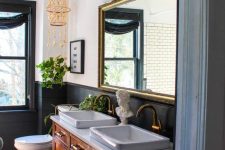 an eclectic bathroom with black paneling, a black window frame, a stained vanity, a large mirror in a gilded frame, a bold rug and sconces