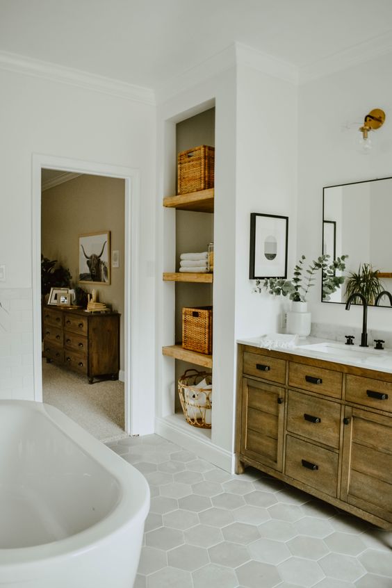 An eclectic boho meets mid century modern bathroom with a wooden vanity, baskets, hex tiles and potted greenery