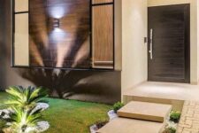an elegant and modern front yard with stone tiles, neutral pebbles, greenery, grass and tropical plants with additional lights
