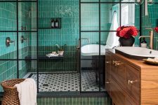 an eye-catchy bathroom with green skinny tiles, black and white hex ones, a stained vanity, a sink and a bathtub is amazing