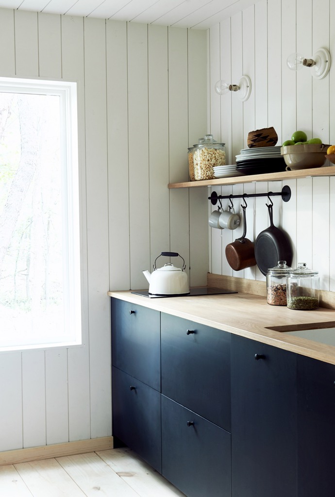 The kitchen is done with sleek navy cabinets, light-colored wooden shelves and countertops and there's much natural light