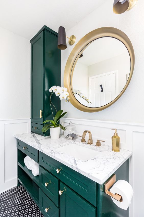 a stunning emerald and white stone bathroom spruced up with gold hardware and a large round mirror