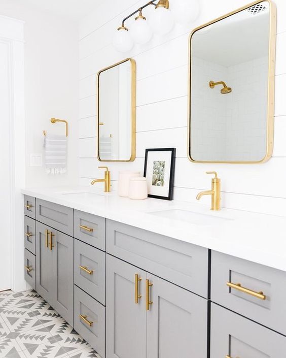 a grey double vanity, a white shiplap wall and gold fixtures, hardware and gold mirror frames
