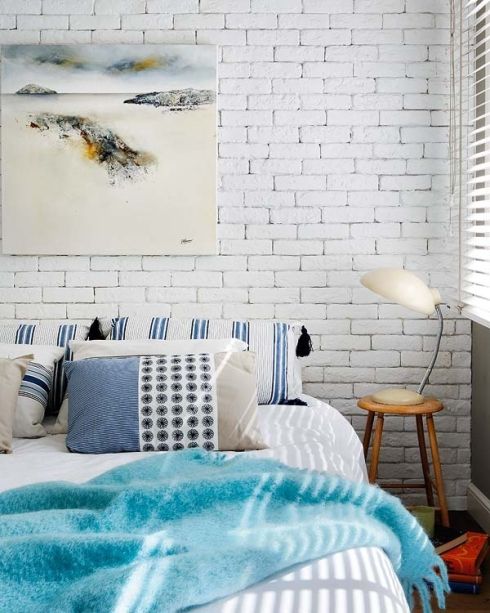 A beach inspired bedroom with a statement white brick wall that highlights the artwork and contrasts the colorful bedding