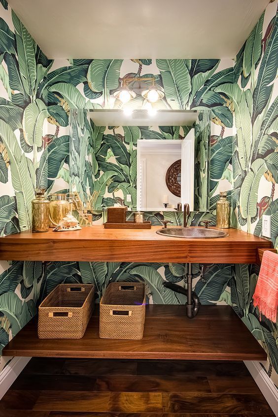 a chic powder room done with bright tropical print wallpaper and wooden items
